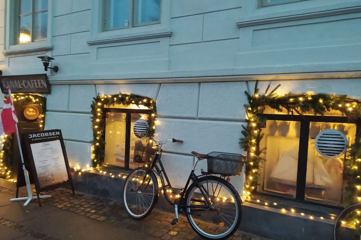 A commuter bike with a basket parked under holiday lights outside a cafe
